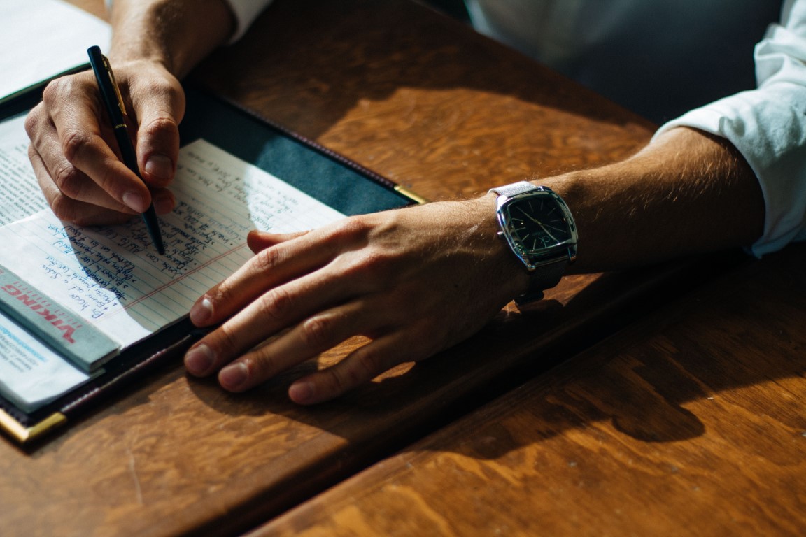 Man taking notes on a wooden desk. Researching your audience is the most important thing you should do before you begin doing content marketing for SaaS.